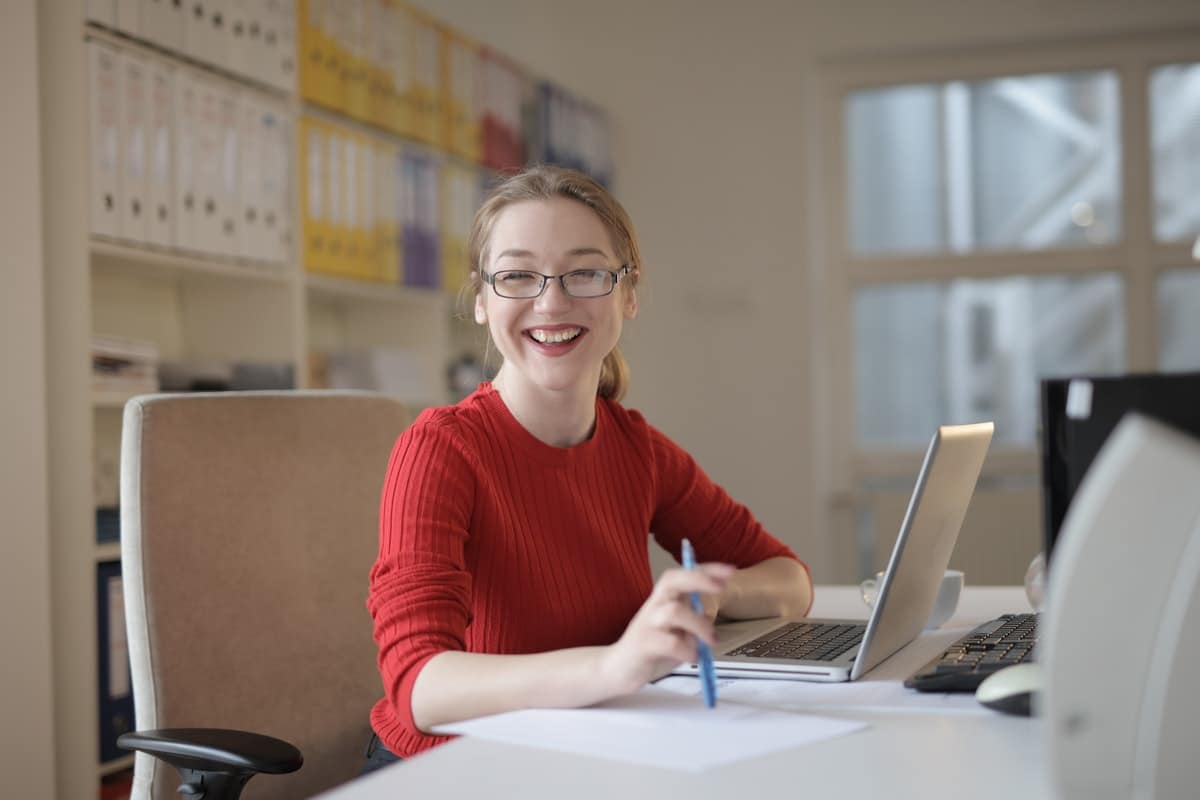 A smiling woman sitting at a desk with a laptop.