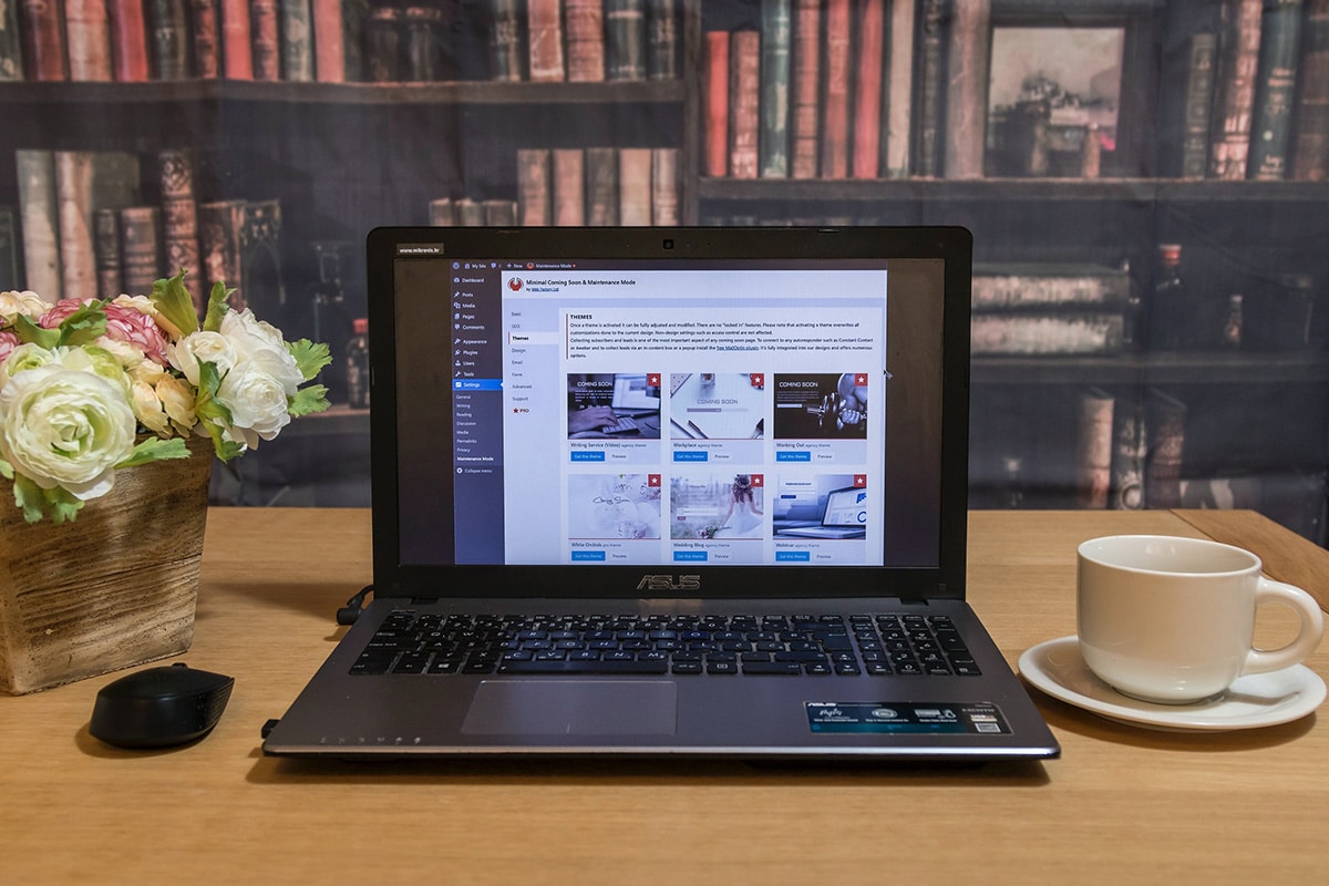 A laptop sits on a table next to a cup of coffee displaying a website.