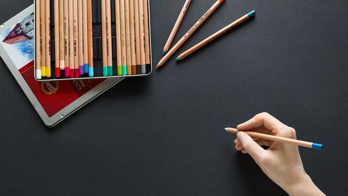 A person is holding a set of colored pencils next to a tablet.