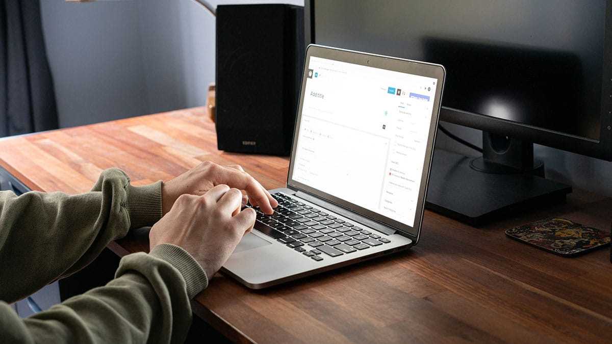 A man using a laptop on a desk and working on a wordpress dashboard.
