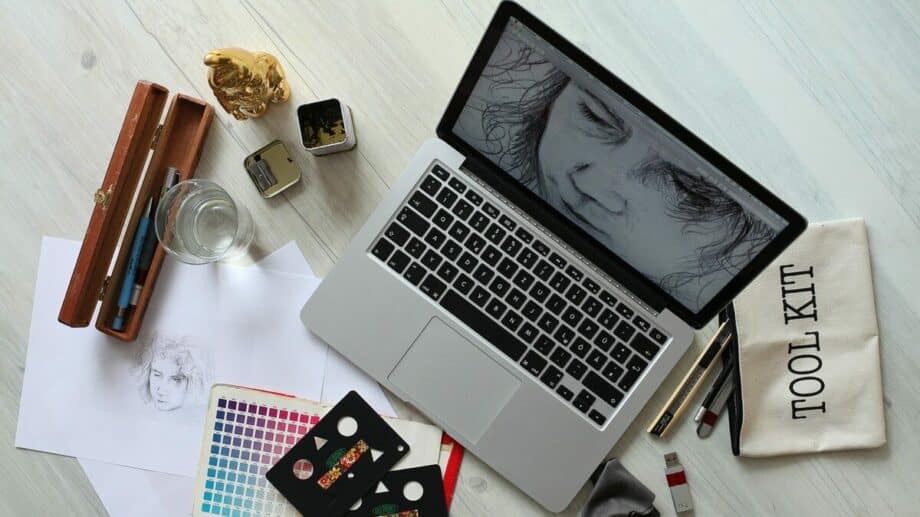 A laptop sits on a table next to art supplies are ready to find some business growth tips for artists.