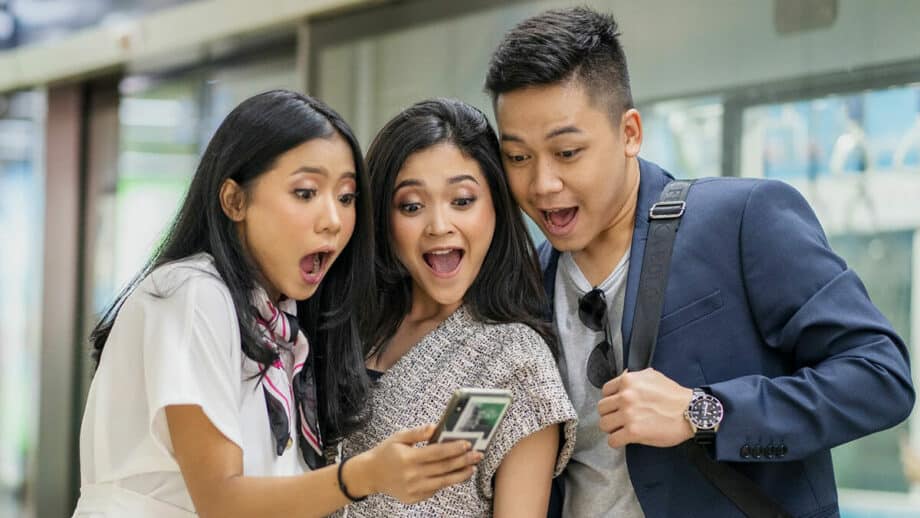 Three asian men and women looking at a cell phone.