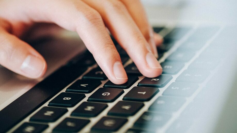 A hand of a person is typing on a laptop keyboard.