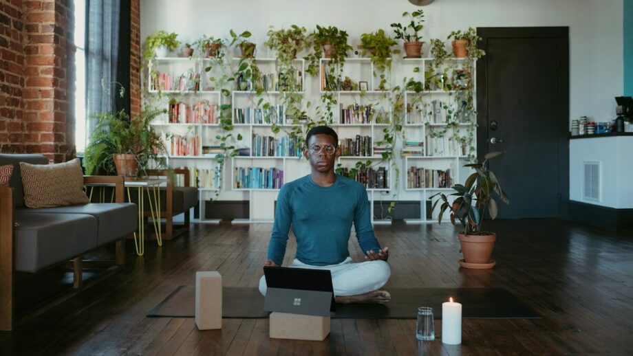 A person is sitting on a yoga mat in a living room with a windows laptop.