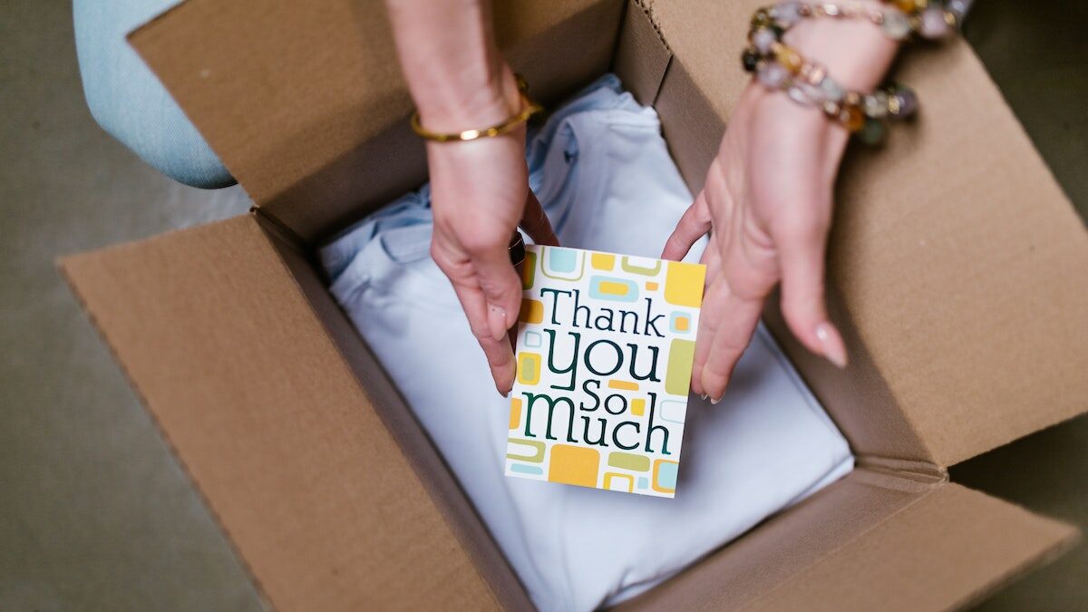 A person opening a box with a thank you card inside.