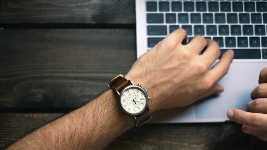 A man is typing on a laptop with a watch on his wrist.