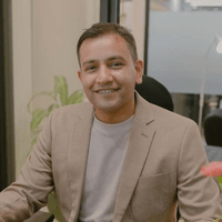 A man named Ronik Patel in a tan suit sitting at a desk.