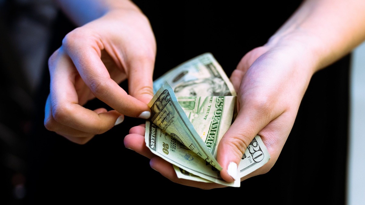 A hand of a woman holding a stack of money.