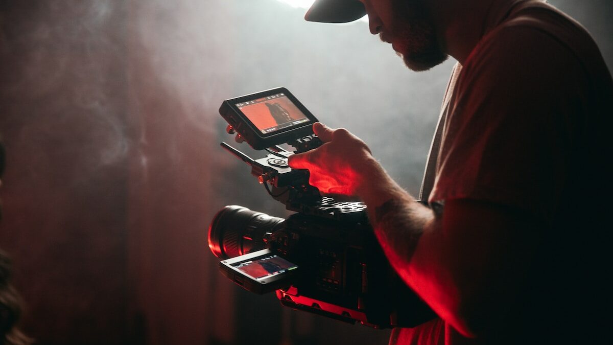 A man holding a video camera in a dark room.