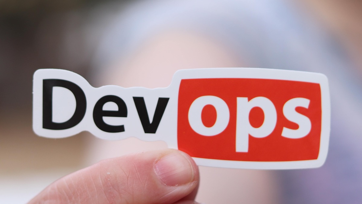 A person holding up a sticker that says devops.