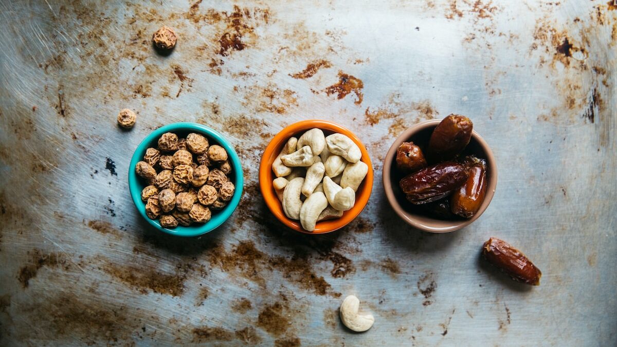 Three bowls of nuts and dates on a metal surface.