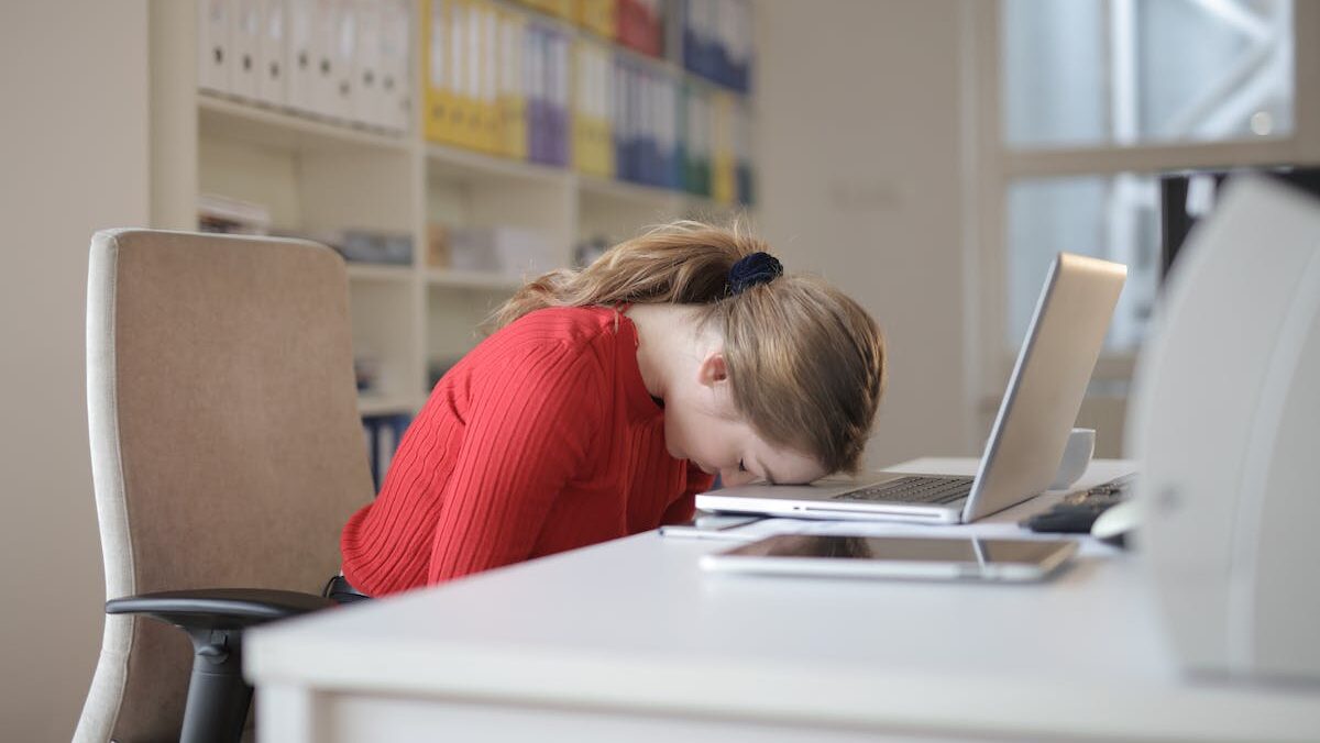 A woman sitting at a desk with her head resting on her laptop.
